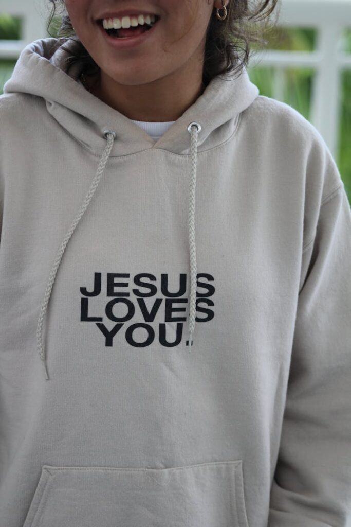 The Art of Drawing Readers In: Your attractive post title goes here Woman wearing a hoodie with 'Jesus Loves You' text, symbolizing faith and casual style.